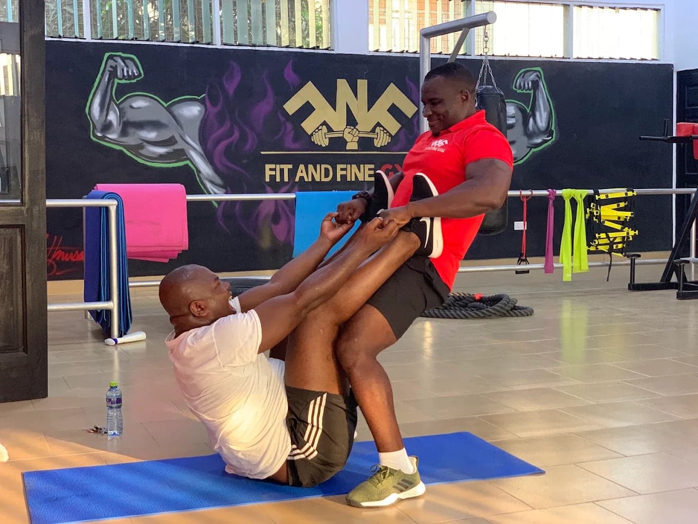 Two people completing an assisted floor exercise inside the gym